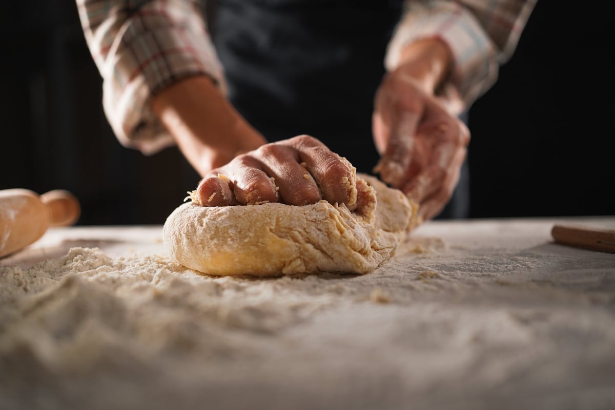 Female prepares pastry, kneads dough on wooden table
