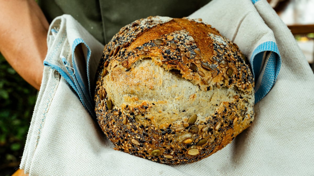 Baker proudly presenting a freshly baked loaf of multigrain bread