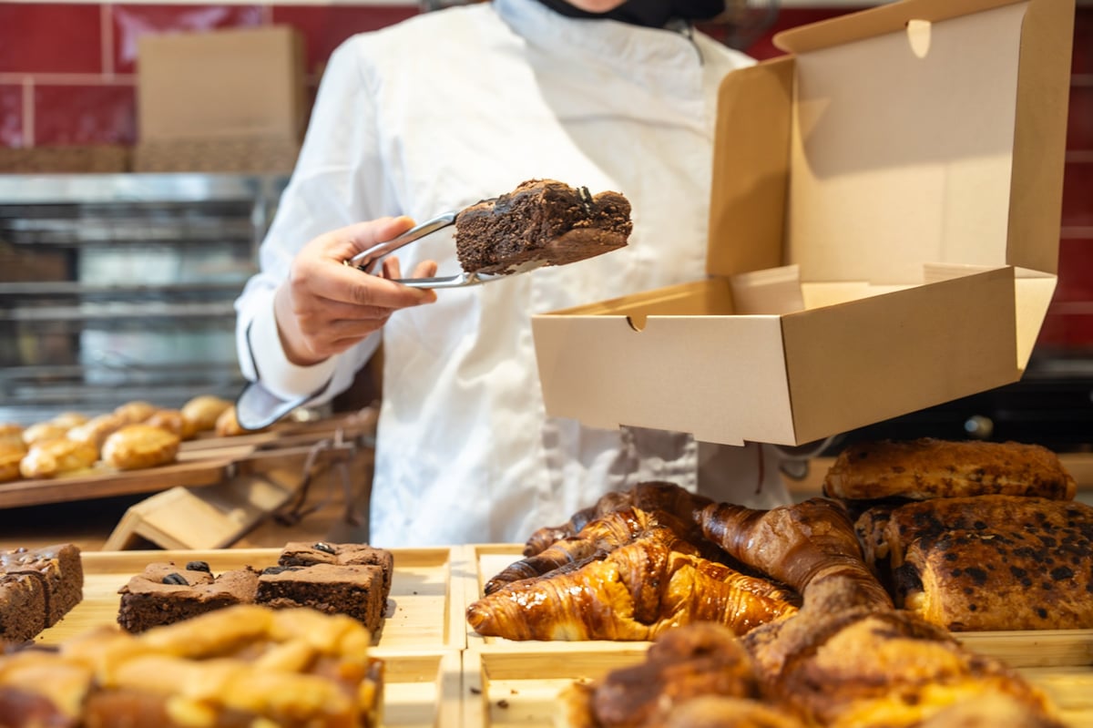 Professional baker packaging a delicious fresh-baked brownie into a small brown takeaway box